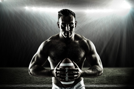 Shirtless American football player with ball against spotlightの写真素材