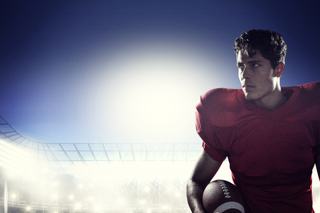 Serious American football player looking away holding ball against rugby stadiumの写真素材