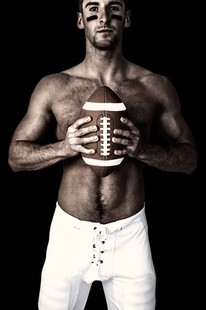 Portrait of shirtless player holding rugby ball against blackの写真素材