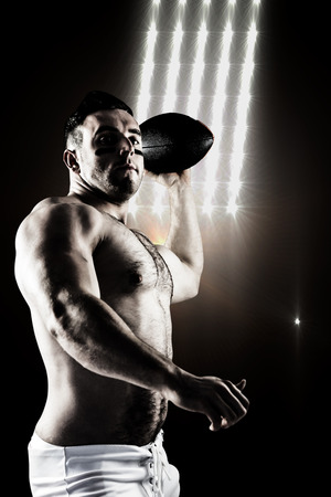 Shirtless American football player with ball against spotlightsの写真素材
