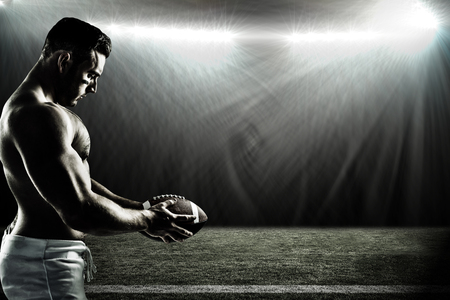 Shirtless American football player with ball against spotlightの写真素材
