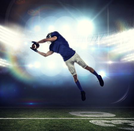 American football player catching ball in mid-air against american football arena