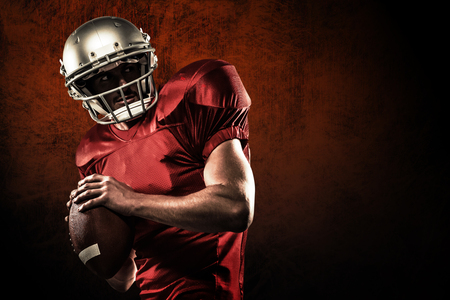 American football player in red jersey looking away while holding ball against dark backgroundの写真素材