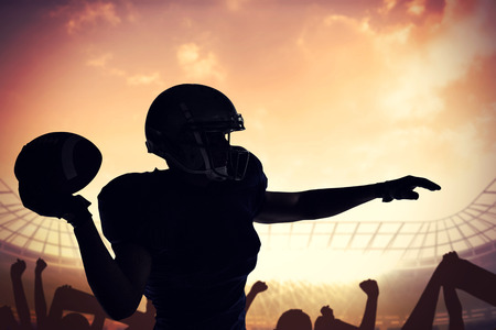 Silhouette American football player throwing ball against football stadium with cheering crowdの写真素材
