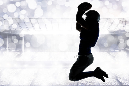 Silhouette American football player jumping while holding ball against glowing backgroundの写真素材