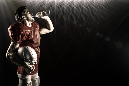 Thirsty American football player in red jersey drinking water  against spotlightsの写真素材