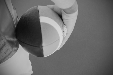 American football player holding the ball  against grey backgroundの写真素材