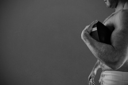 Shirtless American football player with ball against grey backgroundの写真素材