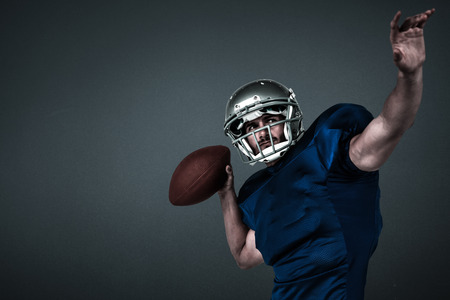 American football player looking away while throwing the ball against teal, blue