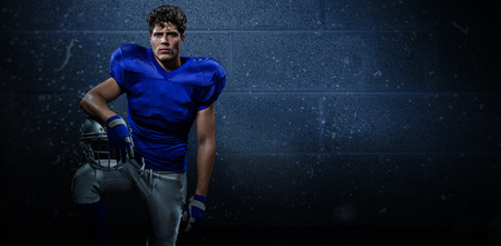 Portrait of determined American football player with hand on helmet against dark grey roomの写真素材
