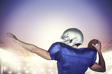 Rear view of American football player throwing ball against rugby stadiumの写真素材