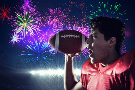 Aggressive sportsman with ball against fireworks exploding over football stadium