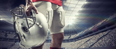 Close-up of American football player in red jersey holding helmet against rugby stadiumの写真素材