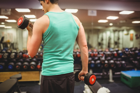 Fit man lifting heavy black dumbbells at the gymの写真素材