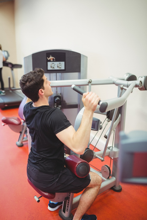 Fit man using weights machine for arms at the gym