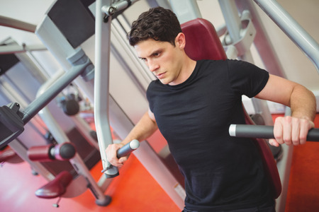 Fit man using weights machine for arms the gym