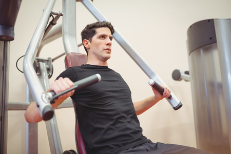 Fit man using weights machine for arms at the gym
