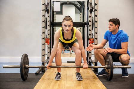 Woman lifting barbell with trainer spotting her at the gymの写真素材