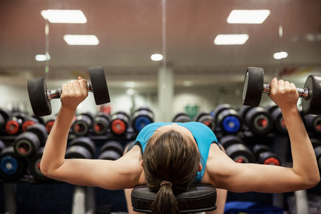 Woman lifting dumbbell weights while lying down at the gym