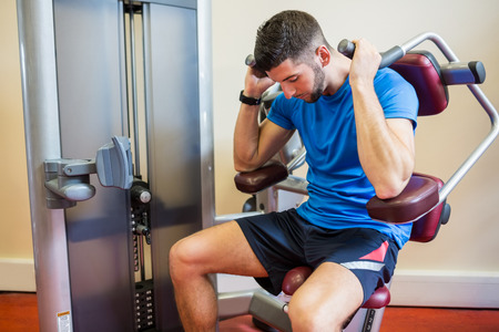 Concentrating man using weights machine at the gym