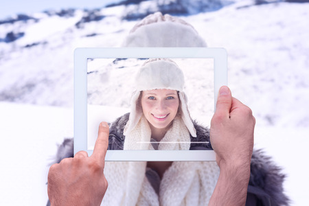 Hand holding tablet pc against woman in warm clothing on snow covered landscape