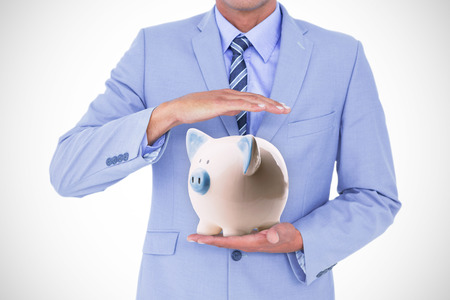Handsome businessman gesturing with hands against piggy bank Handsome businessman gesturing with hands on a white backgroundの写真素材