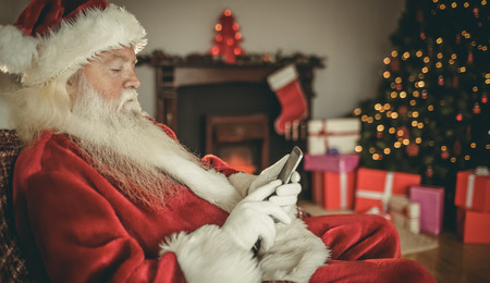 Concentrated santa using smartphone at christmas at home in the living roomの写真素材
