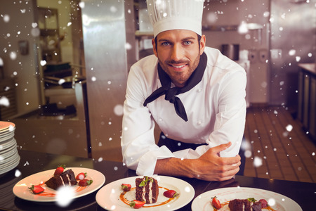 Snow against happy chef looking at camera behind counter of dessertsの写真素材