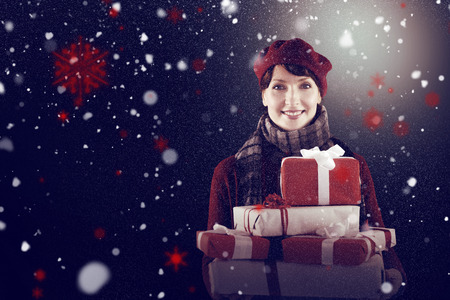 Smiling woman holding large presents against snow
