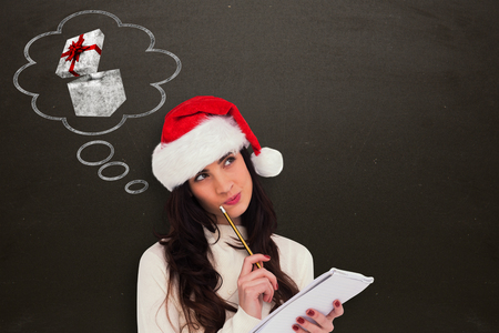 Festive brunette thinking about her christmas list against blackboardの写真素材