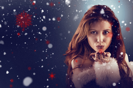 Festive redhead blowing a kiss against snowの写真素材
