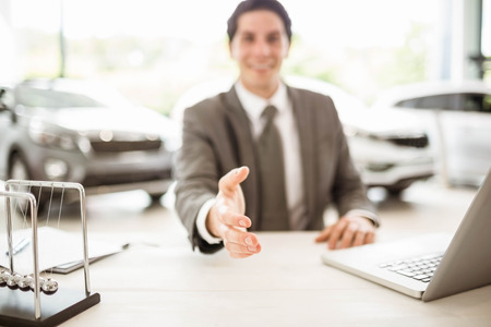 Smiling salesman ready to shake hand at new car showroomの写真素材