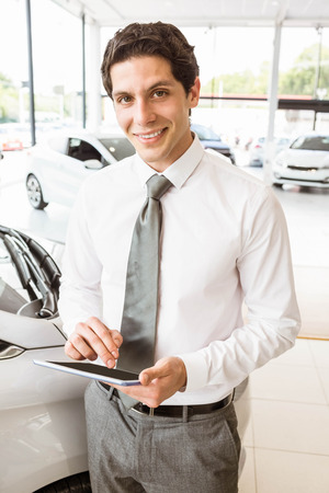 Smiling salesman using tablet near a car at new car showroomの写真素材