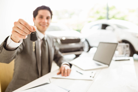 Smiling salesman holding a customer car key at new car showroomの写真素材