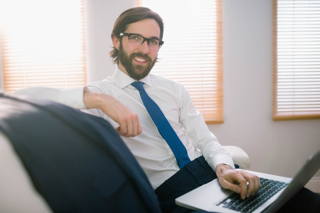 Businessman using laptop on the couch at home in the living roomの写真素材