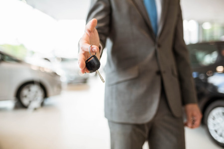 Salesman standing while offering car keys at new car showroomの写真素材