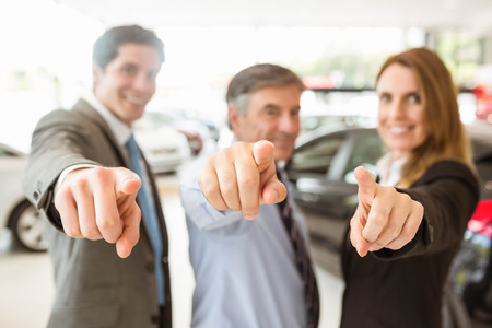 Group of smiling business team pointing together at new car showroomの写真素材