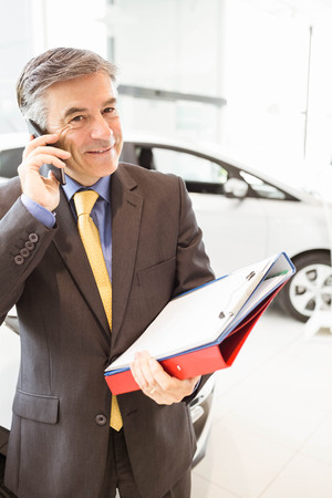 Smiling salesman having a phone call at new car showroomの写真素材