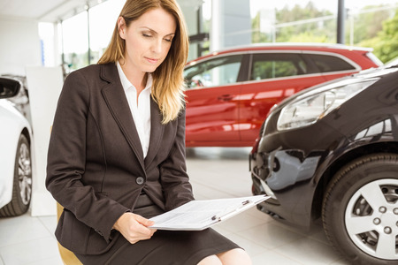 Smiling saleswoman sitting near cars at new car showroomの写真素材