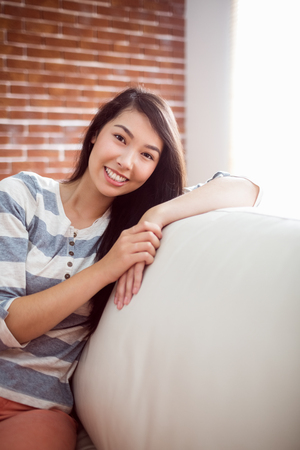 Smiling asian woman on couch at home in the living roomの写真素材