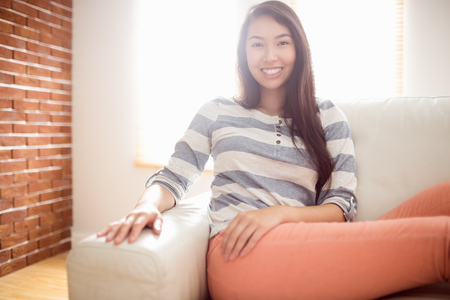 Smiling asian woman on couch at home in the living roomの写真素材