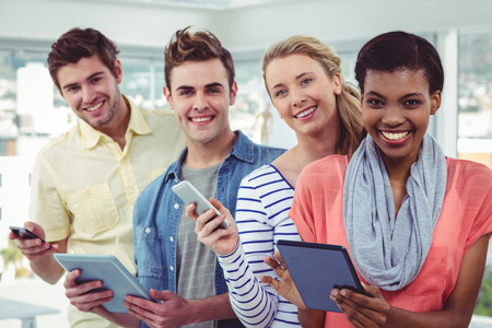 Smiling creative team standing in a line using technology in casual office