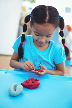 Smiling girl using modelling clay at their deskの写真素材