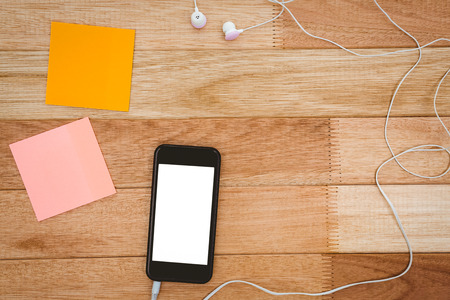 Post it and black smartphone with white headphones on wood deskの写真素材