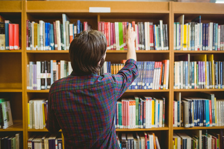 Student picking a book from shelf in library at the universityの写真素材