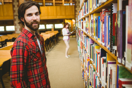 Hipster student picking a book in library at the universityの写真素材