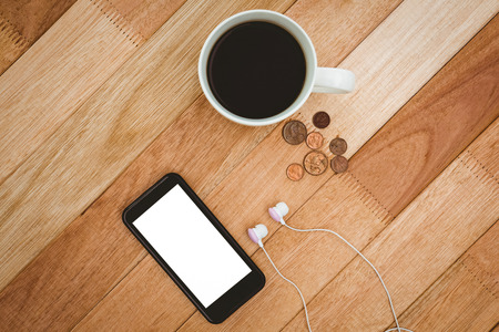 Coffee and black smartphone with white headphones on wood deskの写真素材