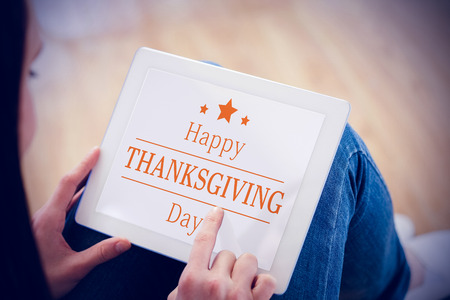 Teen using a tablet pc sitting on the floor against happy thanksgivingの写真素材