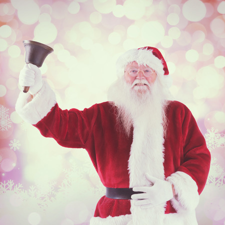 Santa Claus rings his bell against glowing christmas backgroundの写真素材
