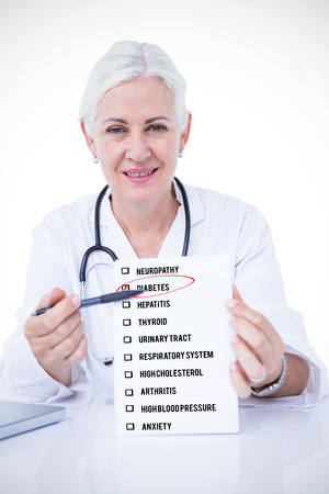 Portrait of smiling female doctor holding notepad and pen at desk against ill health checklistの写真素材